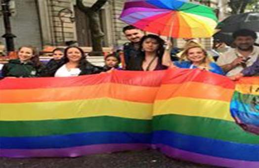 Maria Jose Lubertino junto a otras personas marchando por los derechos LGTTTBIQ tomando una bandera con los colores de la diversidad