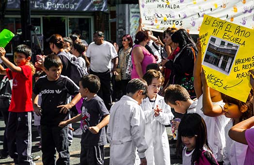 Niñez con guardapolvo en la puerta de una escuela, manifestación por mejoras en la educación