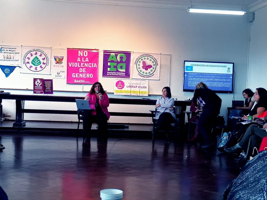 Mujer con micrófono y notebook sentada brindando una charla en la Jornada de Interseccionalidad en el acceso a la Justicia